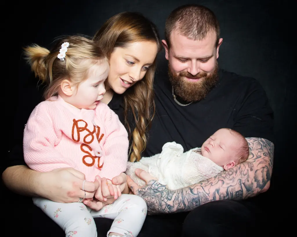 a mum, dad and older daughter welcome a newborn into their family at a professional photo shoot