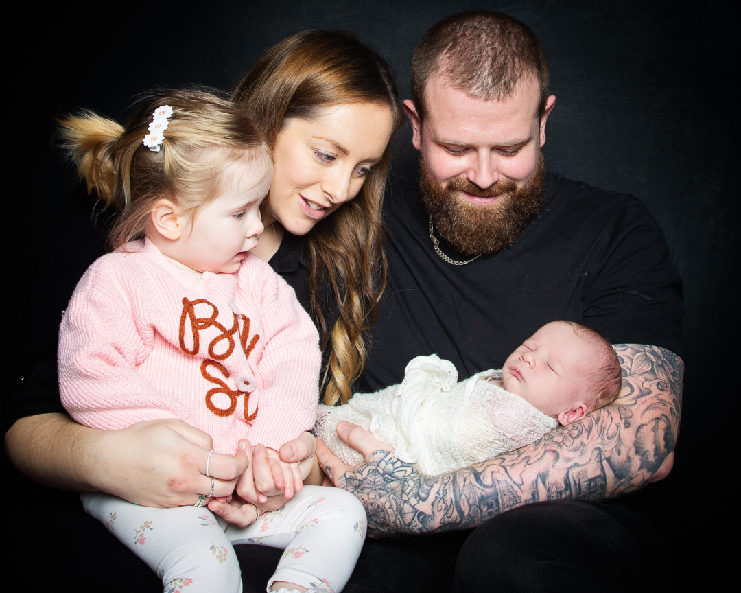 a mum, dad and older daughter welcome a newborn into their family at a professional photo shoot