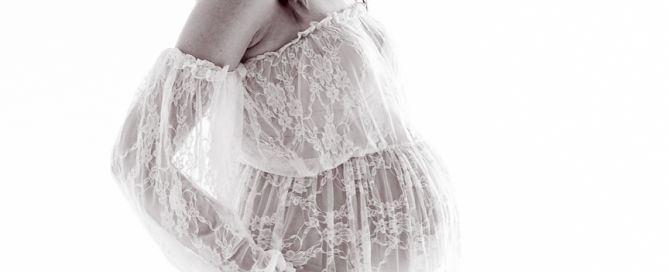 a pregnant woman wearing a white lace dress at a professional maternity portrait shoot