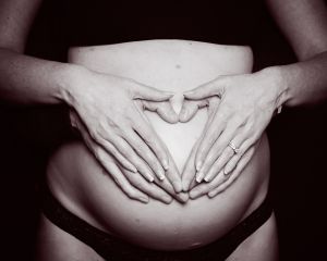 Parents hands making the shape of a heart on a black and white image of a pregnant belly at a professional photo shoot