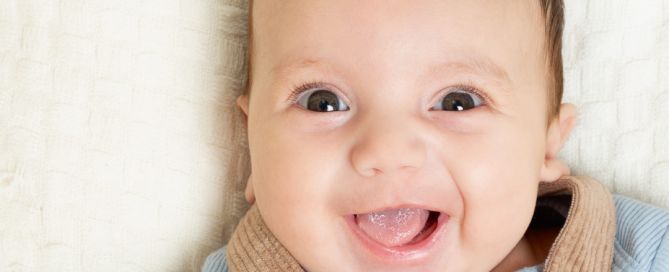 a happy baby boy in beige dungarees smiles up at the camera