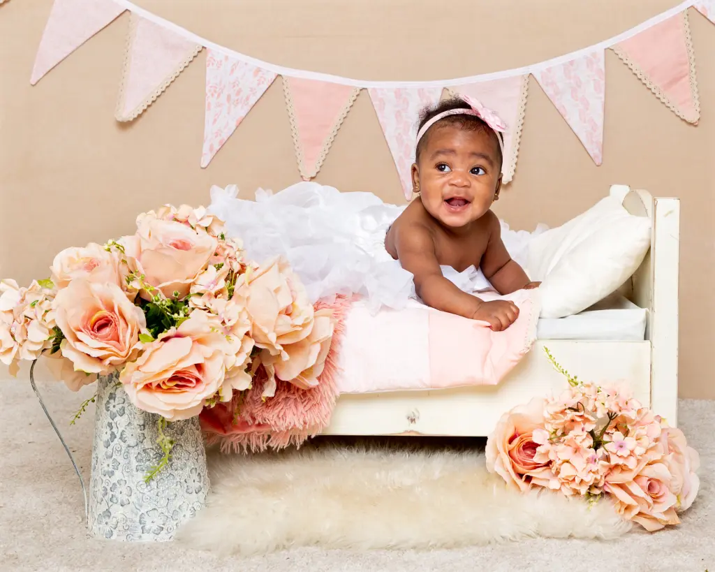 Baby Photography East Grinstead West Sussex a little girl on a miniature white bed with peach flowers and a cream backdrop