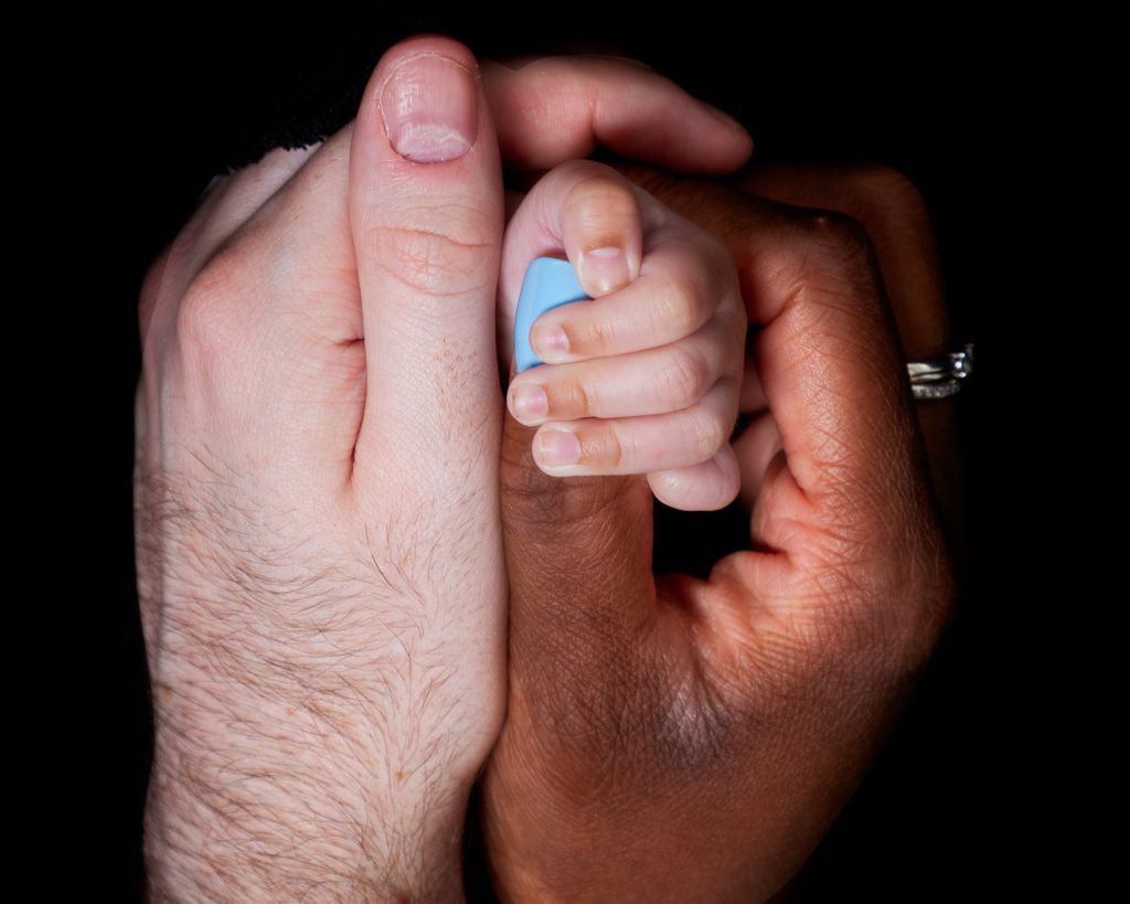 Newborn Photography East Grinstead West Sussex A newborn close up shot of the baby's hand wrapped around mum's thumb with dads hand holding them.