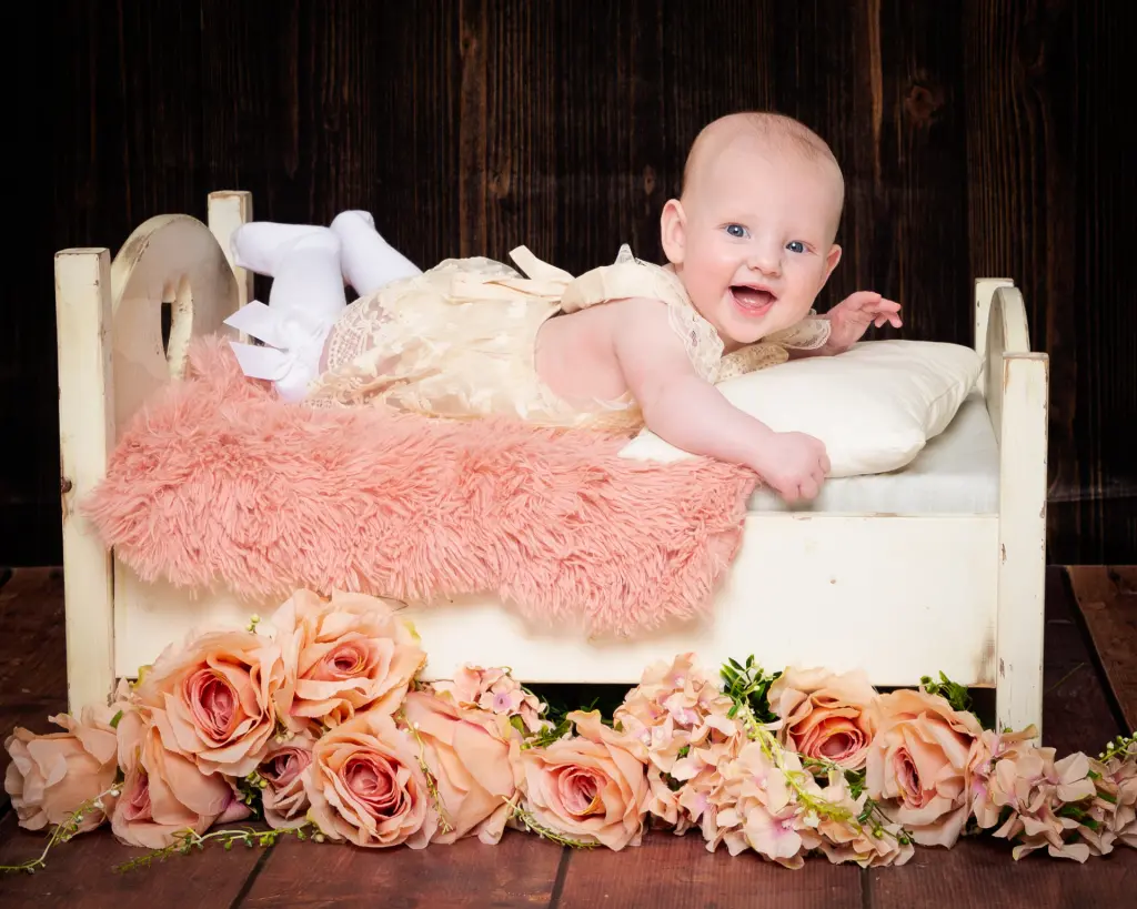 Baby Photography East Grinstead West Sussex a little girl on a miniature white bed with peach flowers and a dark backdrop