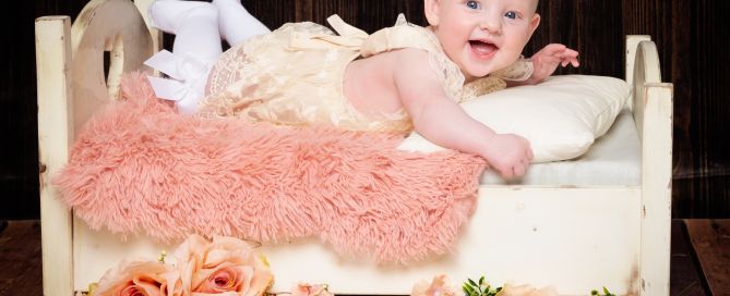 a little girl on a miniature white bed with peach flowers and a dark backdrop