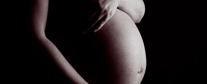 a black and white image of a pregnant person cradling her bare belly