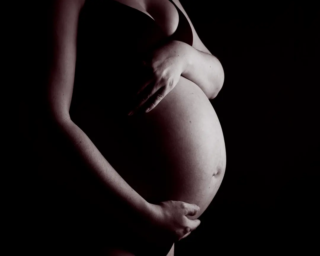a black and white image of a pregnant person cradling her bare belly
