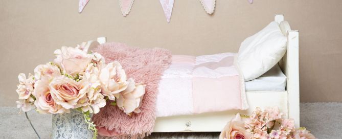 a mini white bed styled with peach quilt and accessories