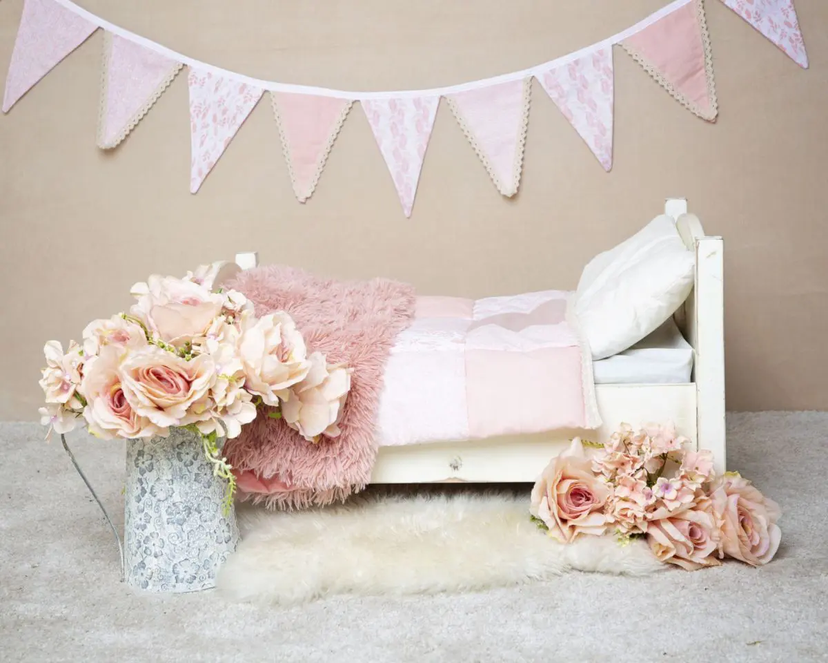 a mini white bed styled with peach quilt and accessories