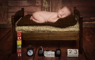 A baby sleeps on their tummy on a dark wooden bed