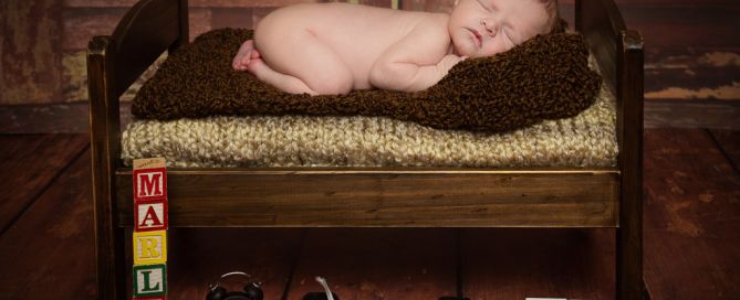 A baby sleeps on their tummy on a dark wooden bed