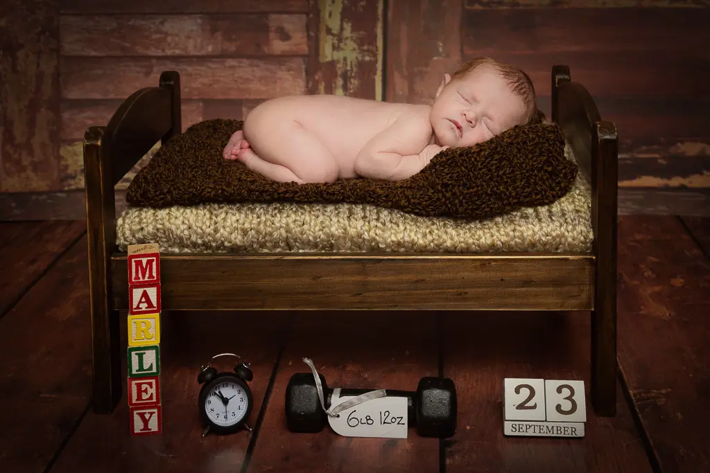 A baby sleeps on their tummy on a dark wooden bed