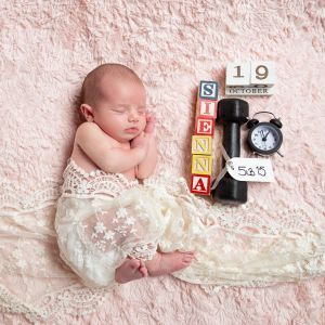 a newborn baby posed next to birthday annoucement items.