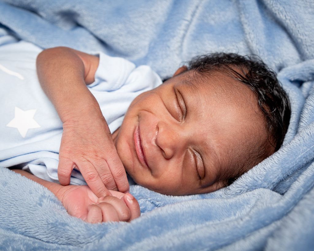 A smiling newborn asleep wrapped in a blue blanket