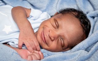 A smiling newborn asleep wrapped in a blue blanket