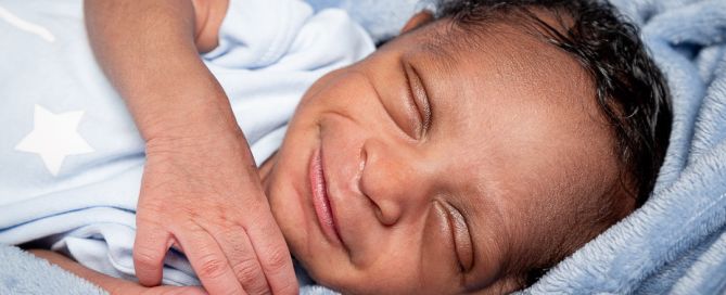 A smiling newborn asleep wrapped in a blue blanket