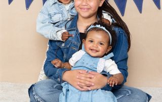 Three sisters pose in the studio in front of a cream backdrop wearing denim
