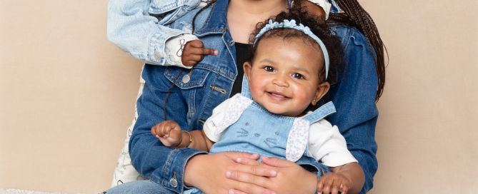 Three sisters pose in the studio in front of a cream backdrop wearing denim