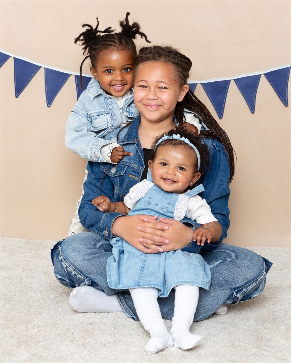 Three sisters pose in the studio in front of a cream backdrop wearing denim