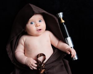 A baby wrapped in a Jedi robe with a lightsaber