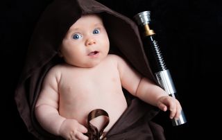 A baby wrapped in a Jedi robe with a lightsaber