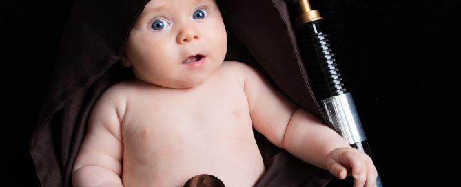 A baby wrapped in a Jedi robe with a lightsaber