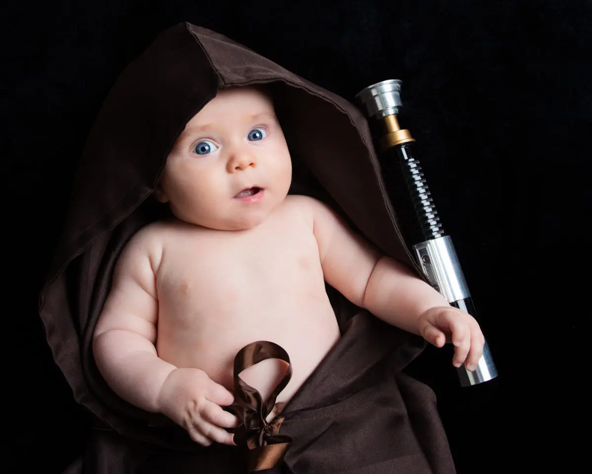 A baby wrapped in a Jedi robe with a lightsaber