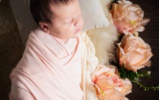 a little girl swaddled in peach sleeps on a bed with peach flowers beside her