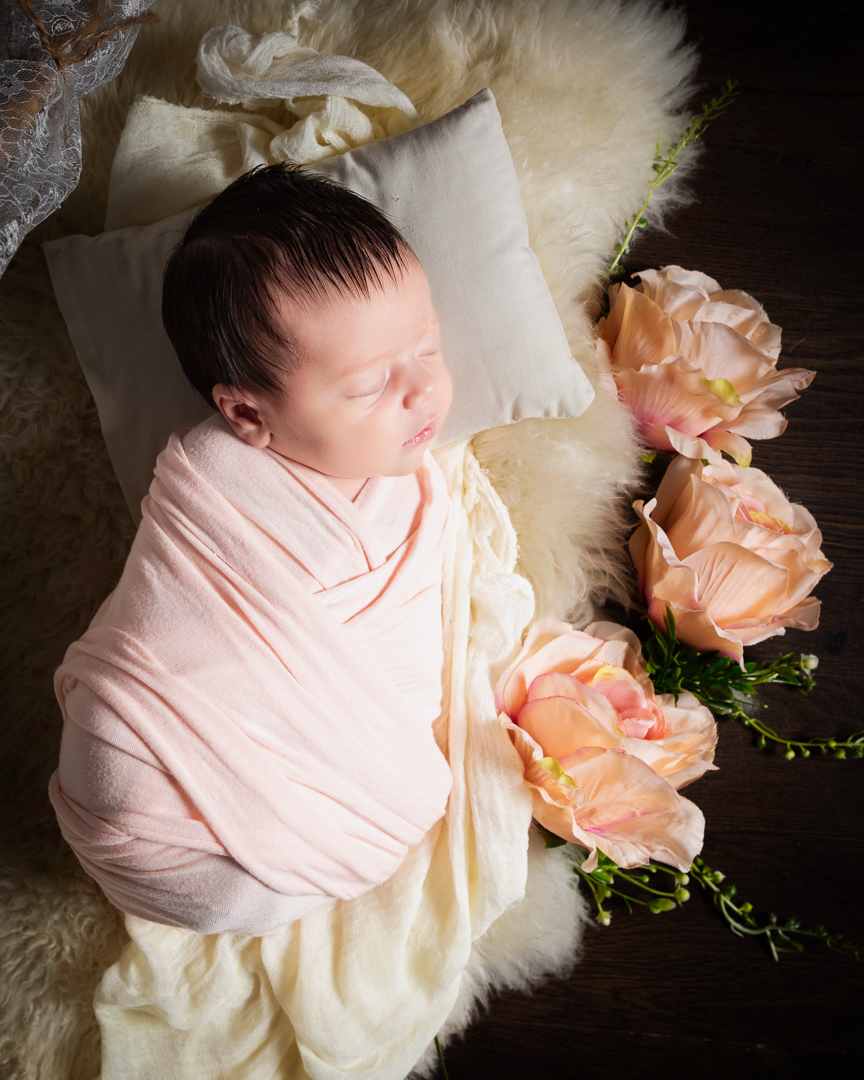a little girl swaddled in peach sleeps on a bed with peach flowers beside her