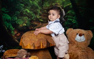 a little boy poses in a woodland set up surrounded by tedeies having a picnic