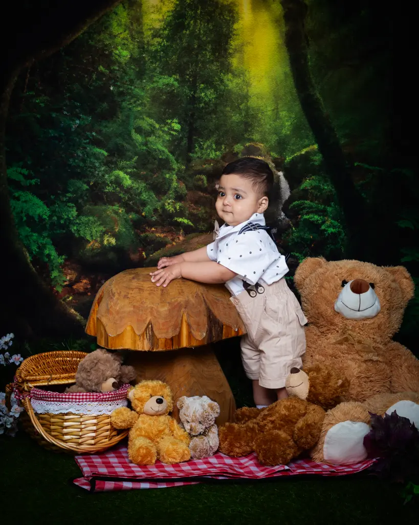 a little boy poses in a woodland set up surrounded by tedeies having a picnic