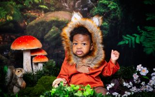a little boy in a fox outfit poses at a photo shoot in a woodland scene