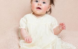 a little girl sitting propped on a beanbag in a christening dress