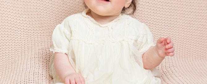 a little girl sitting propped on a beanbag in a christening dress