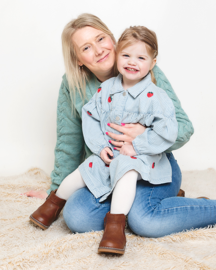 a little girl sits on her mums lap at a professional photo shoot