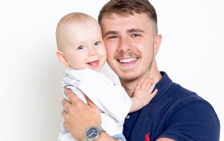 a dad and his baby son are photographed in the studio both smiling cheeks pressed together