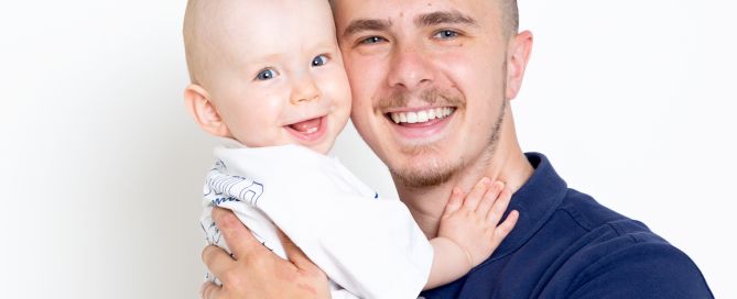 a dad and his baby son are photographed in the studio both smiling cheeks pressed together