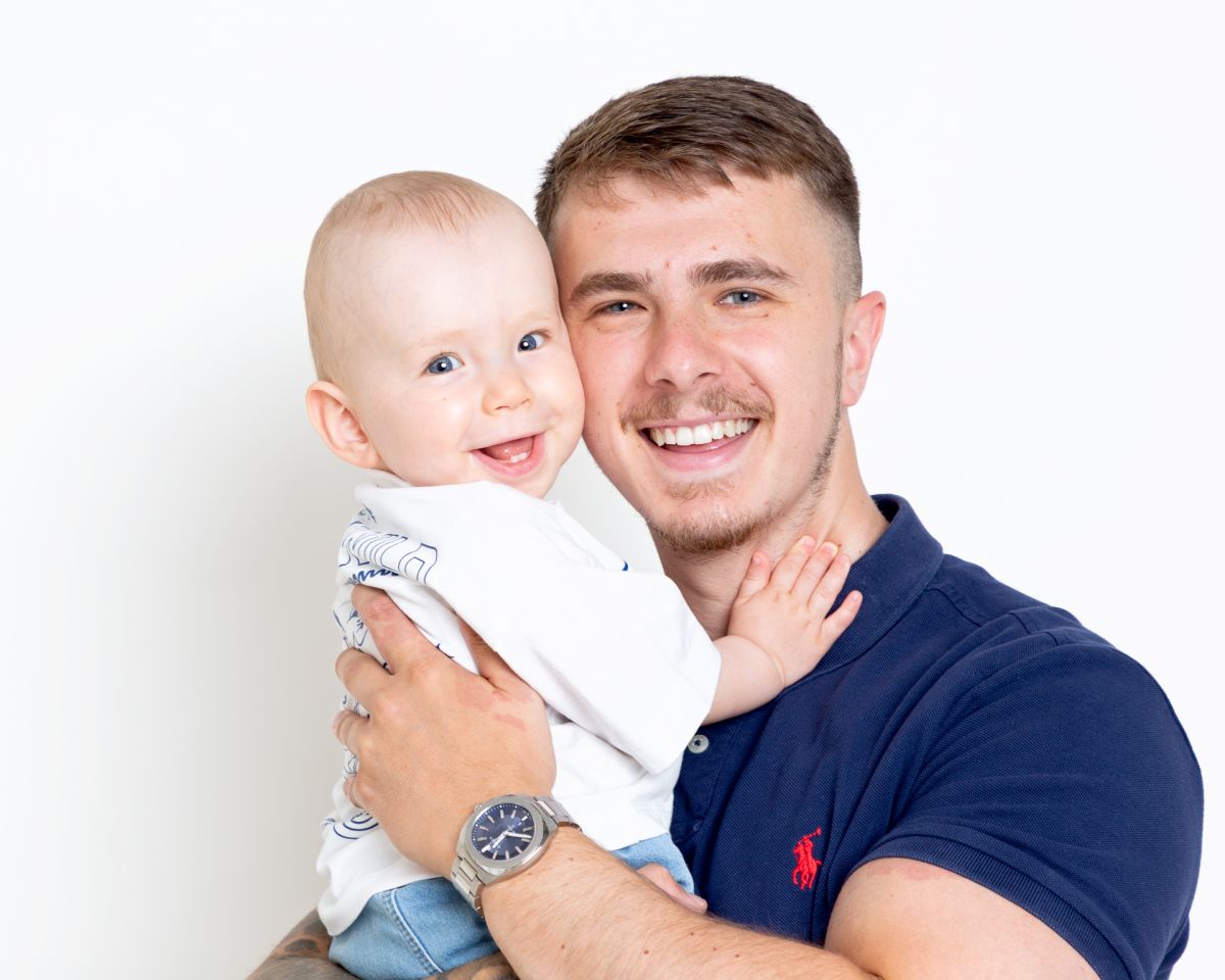 a dad and his baby son are photographed in the studio both smiling cheeks pressed together