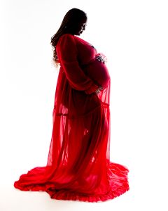 A woman poses in a flowing red maternity dress lit in silhouette