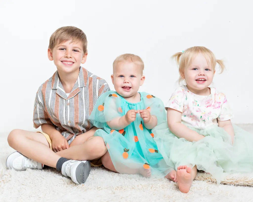 Family Portrait Photo Shoot East Grinstead West Sussex A big brother poses for a portrait photo with his two little sisters and they're all smiling.