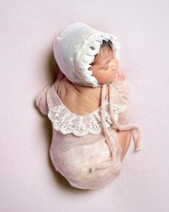 A newborn sleeping on her tummy in a peach lace outfit with matching bonnet