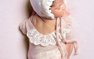 A newborn sleeping on her tummy in a peach lace outfit with matching bonnet