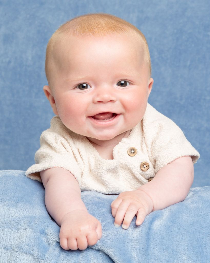 A smiling baby boy in a cream romper on a blue blanket