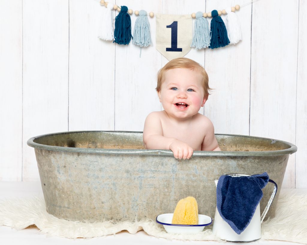 First Birthday Photo Shoot West Sussex a little boy sits in a tin tub with white and blue enamel props