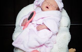 A sleeping newborn wearsa a pink bathrobe and a towel on her head and is relaxing on a spa chair