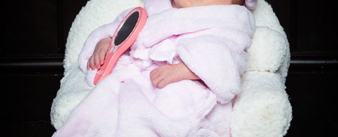 A sleeping newborn wearsa a pink bathrobe and a towel on her head and is relaxing on a spa chair