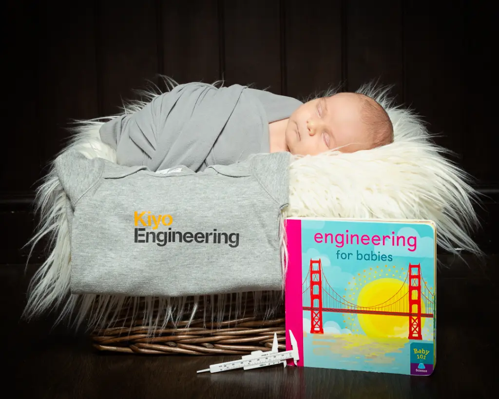 a baby wrapped in a swaddle sleeps in a basket with a book called engineering for babies
