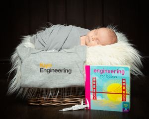 Newborn Photography East Grinstead West Sussex a baby wrapped in a swaddle sleeps in a basket with a book called engineering for babies