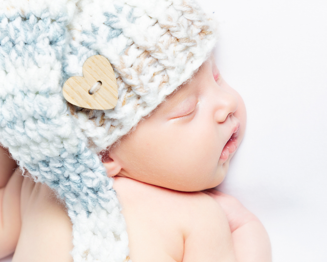 a newborn lies on their front wearing a grey hat with their head turned to the side.