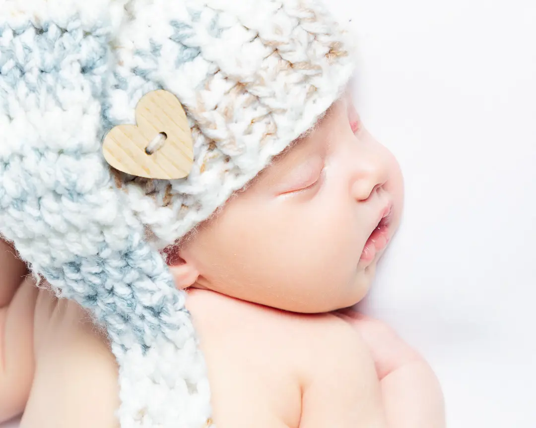 a newborn lies on their front wearing a grey hat with their head turned to the side.